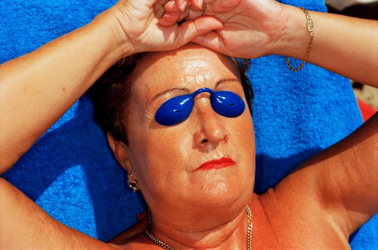 Martin Parr, Benidorm, Spain (1997) aus der Serie Common Sense (1995–1999): Sonnenbadende Urlauberin mit blauen Augenschutzschalen am Strand von Benidorm. © Martin Parr / Magnum Photos