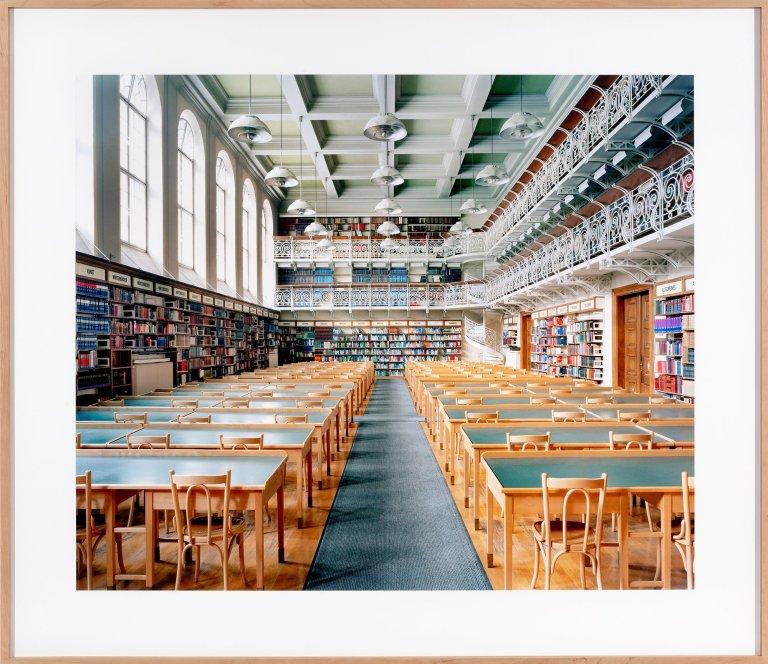 Candida Höfer, Universitätsbibliothek Innsbruck I, 2004 – Fotografie des historischen Lesesaals der Universitätsbibliothek Innsbruck mit Bücherregalen und langen Tischreihen.